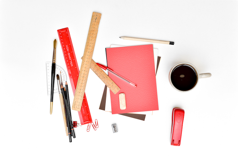 This is an image of disorganised stationery, all arranged in a mess with a cup of coffee and a red stapler the only things 'in order' on the left.