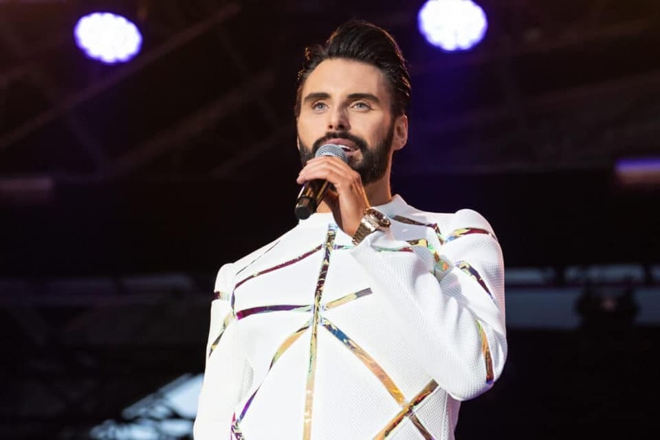 A photo of Rylan Clark, on stage singing in to a microphone.
