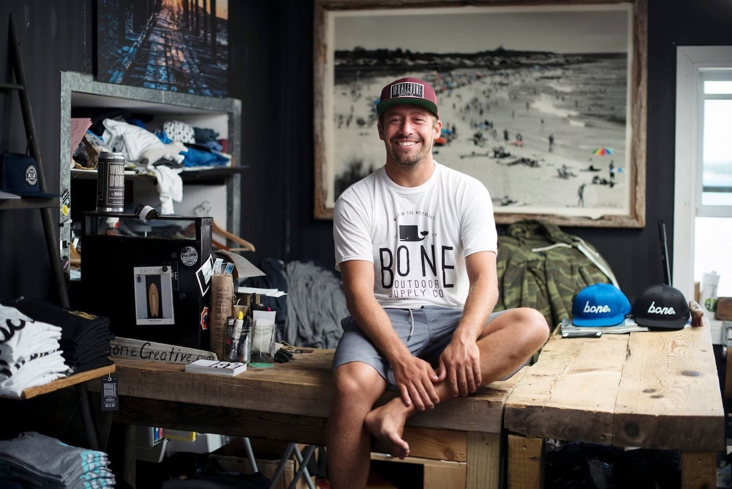 Image shows Whalebone Magazine founder, Jesse Joeckel, smiling and sitting on a table in his lounge-come-office.