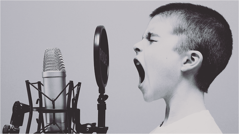This is a black and white side-on image of a young white boy with a shaved head shouting with his eyes shut into a black mouthguard and microphone.