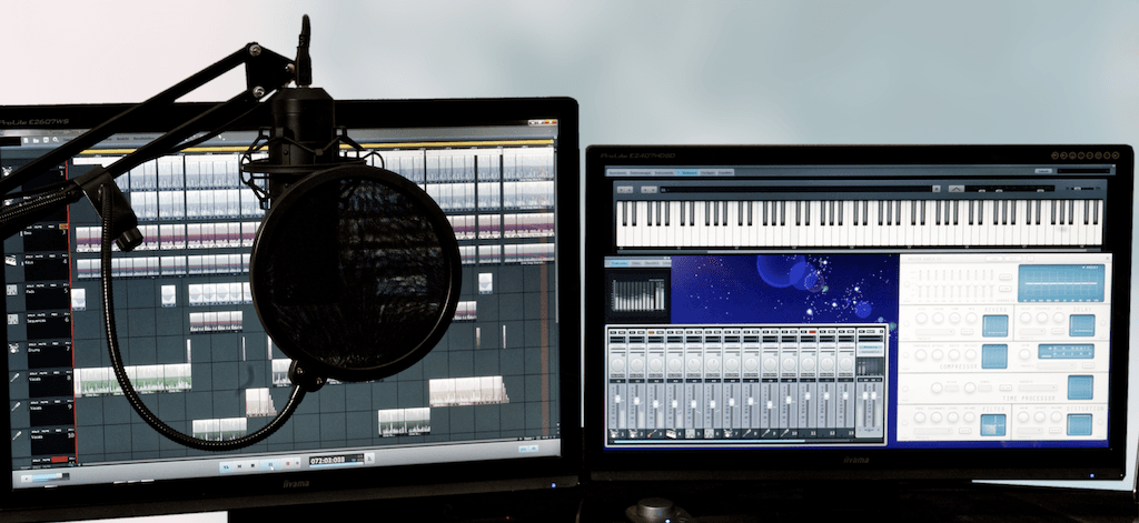 Image shows two computer screens side by side, with different music and audio software on display. In front of the screen is a microphone suspended with a boom arm.